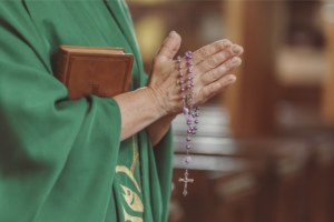 Close up on a priest's hands praying with rosary beads