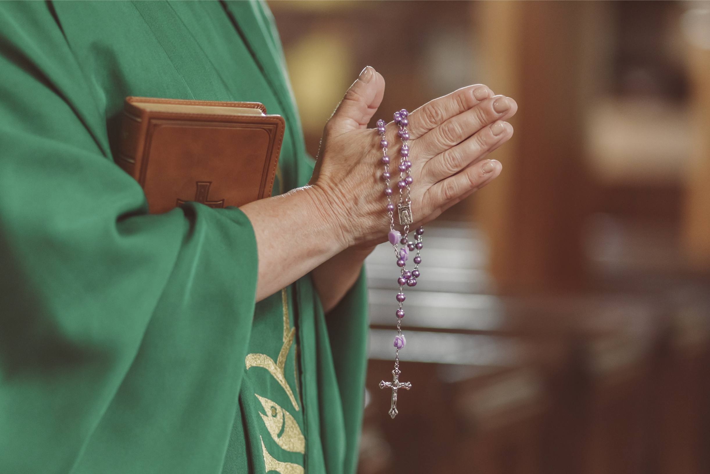 Close up on a priest's hands praying with rosary beads