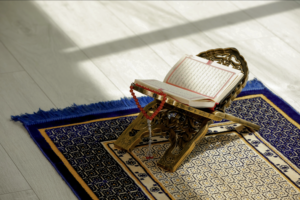 A Quran sitting open on a Rehal on a prayer mat