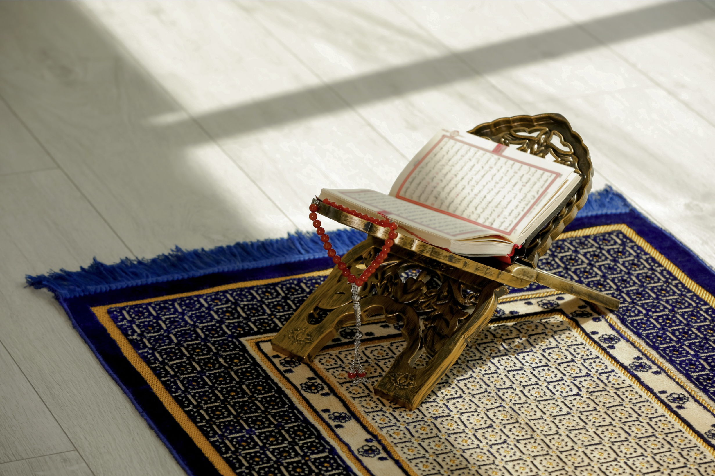 A Quran sitting open on a Rehal on a prayer mat