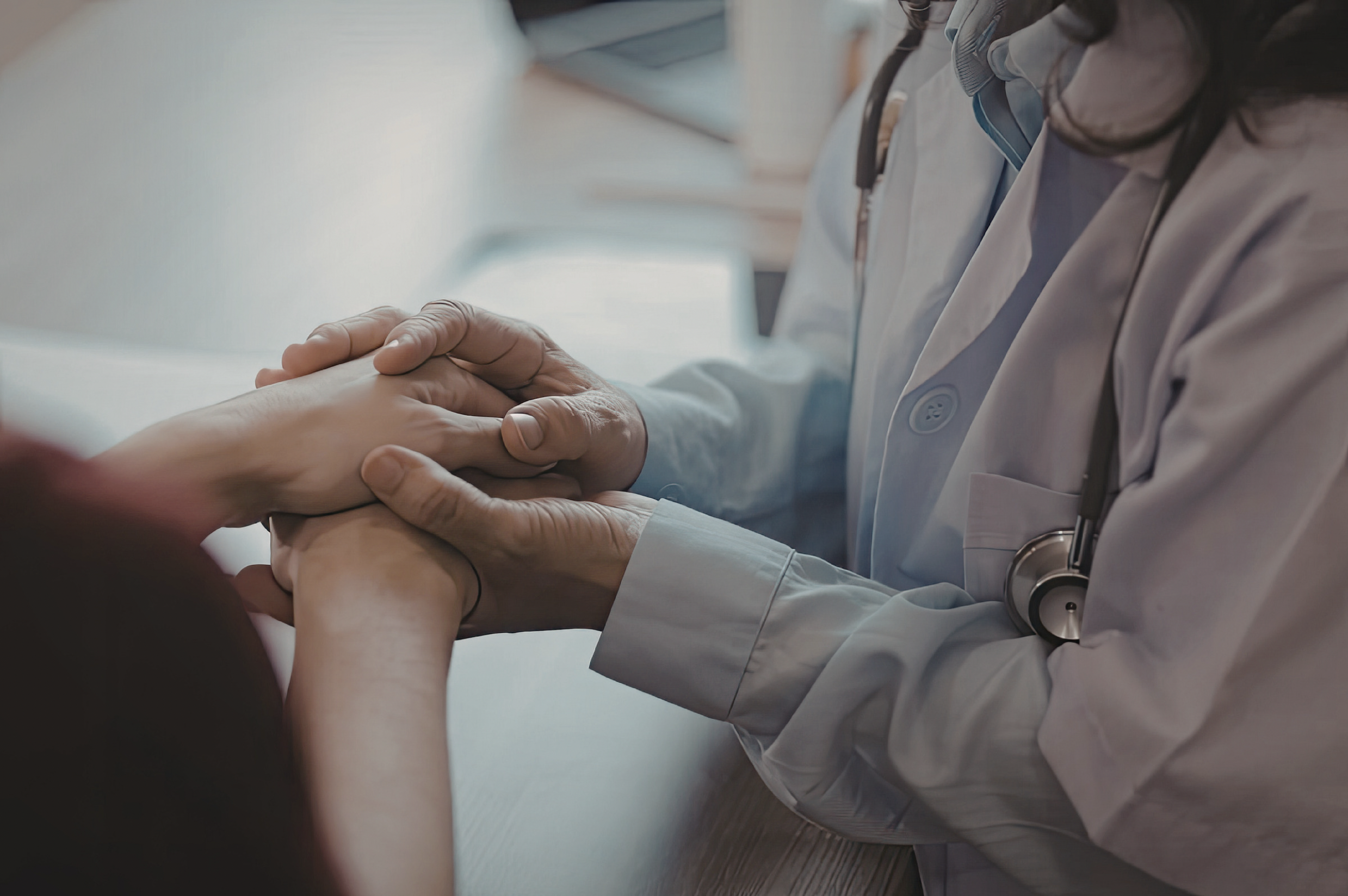A female provider holding her hands comfortingly over a patient's hands