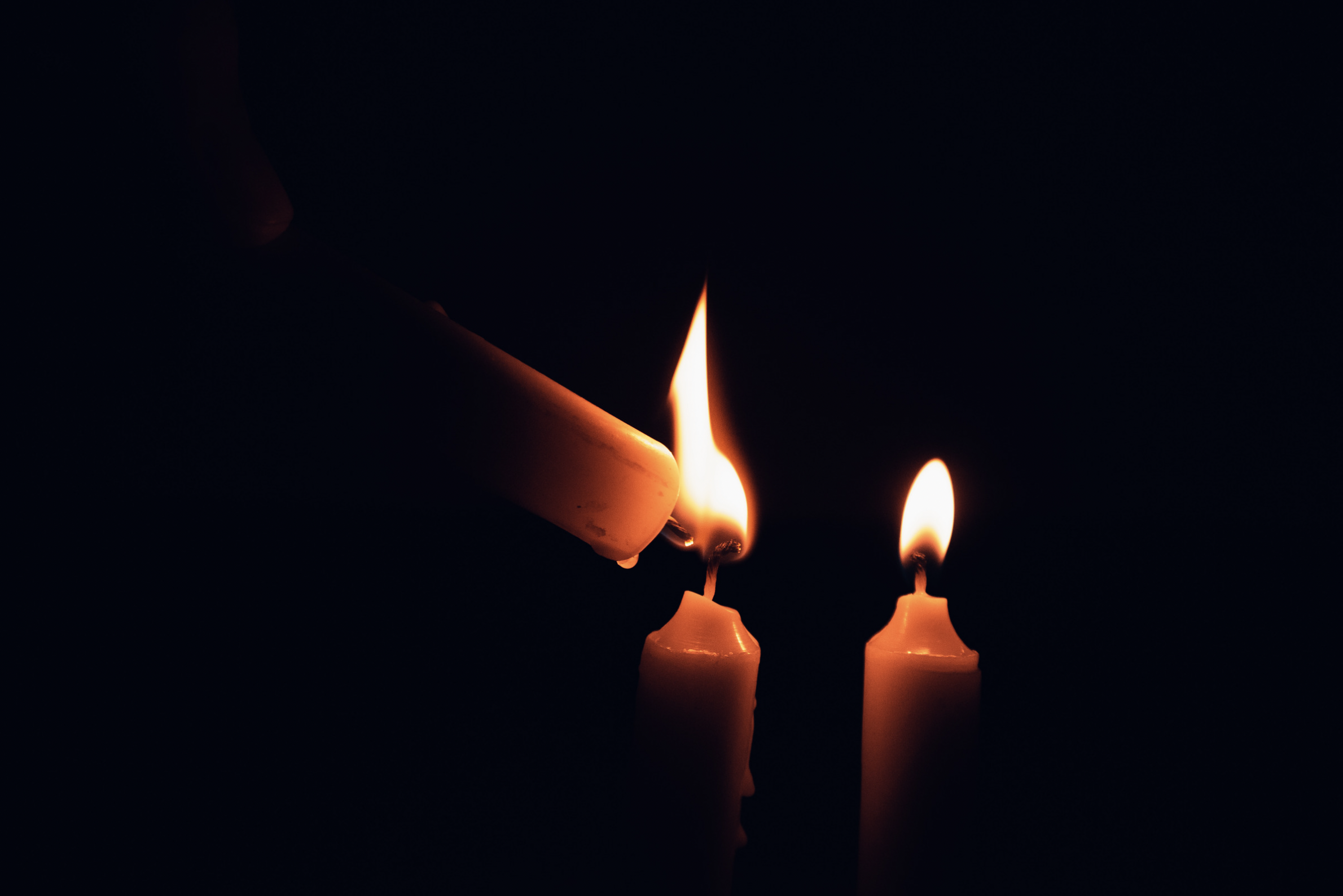 Close up on one prayer candle being used to light to other prayer candles