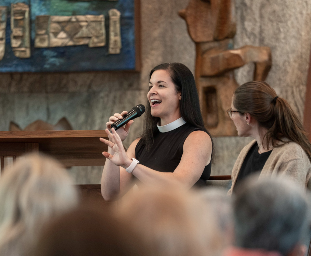 Woman speaking into a podcast mic to a crowd of listeners