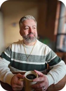 Man smiling with grey hair and beard holding a coffee mug