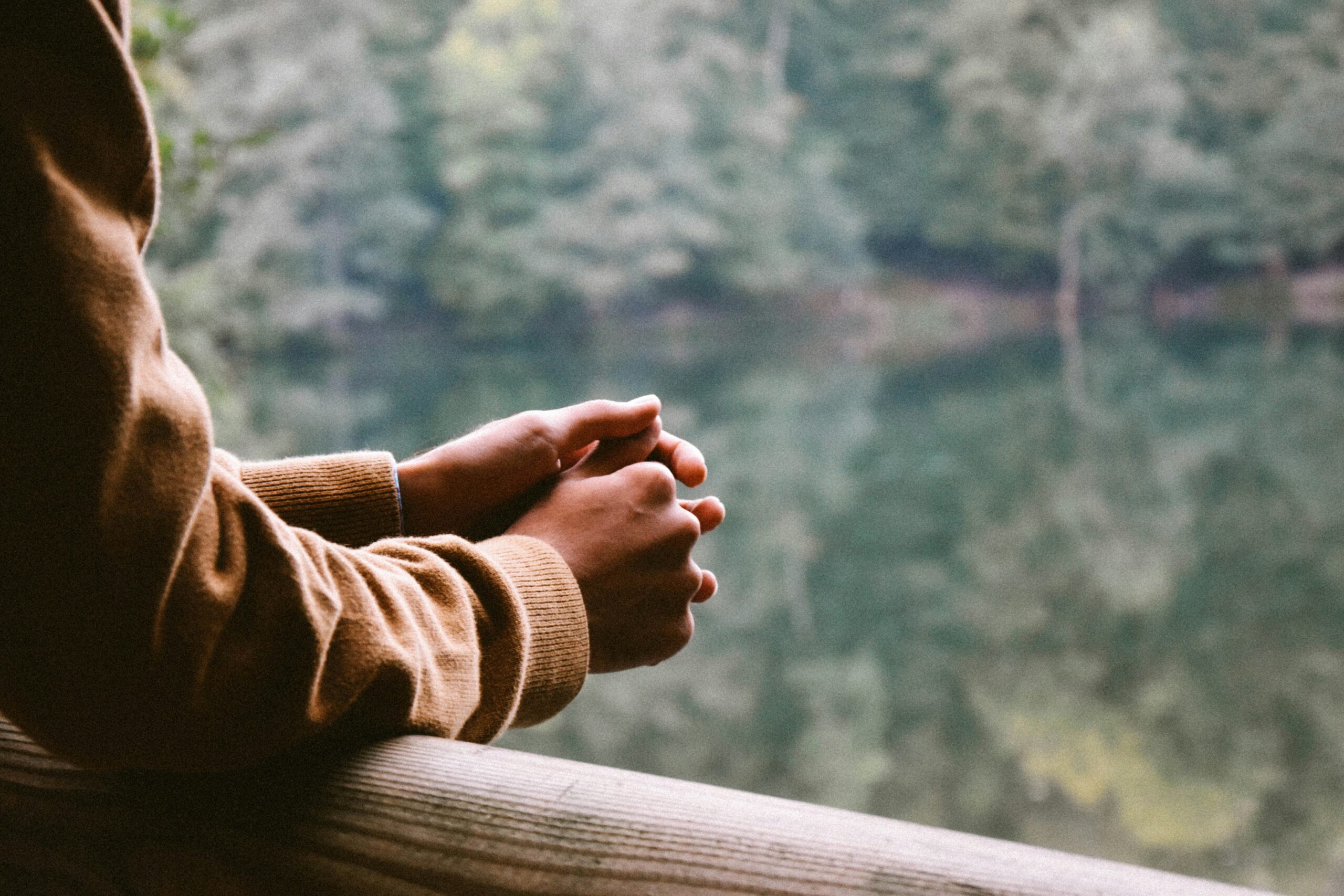 A close up of a person's hands gently clasped as they look out over a peaceful lake